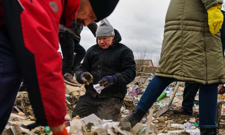 Los residentes locales ayudan a un hombre a limpiar los escombros de una casa que fue destruida por un presunto ataque aéreo ruso.