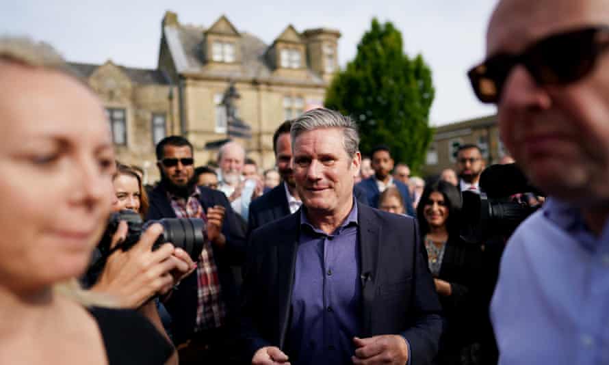 Keir Starmer en medio de un grupo de personas, sonriendo.  Él está enfocado mientras que las personas más cercanas a la cámara no lo están.
