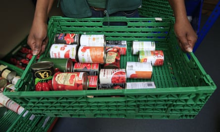 Un trabajador del banco de alimentos sostiene un recipiente de plástico verde con varias latas de ciruelas y tomates picados