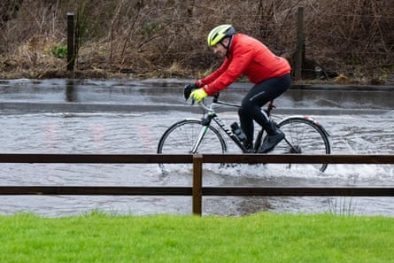 Un ciclista de carretera decidido en medio de las inundaciones en la carretera A81 cerca de la destilería Glengoyne debido al agua de lluvia que cae de la cumbre de Dumgoyne después de las fuertes lluvias anteriores.  