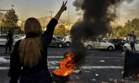 Mujer haciendo un gesto de V mientras quema un fuego en una calle de Teherán.