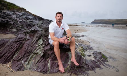 Andy Stewart, guardabosques de Polzeath Beach, sentado en una roca con la playa detrás de él.